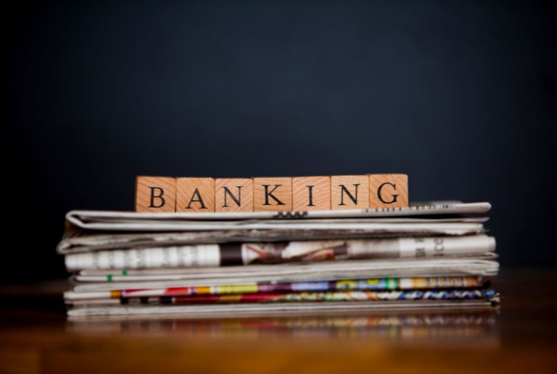 Wooden letter blocks spelling BANKING on a stack of newspapers, representing correspondent banking AML risk and regulatory scrutiny of payable-through accounts